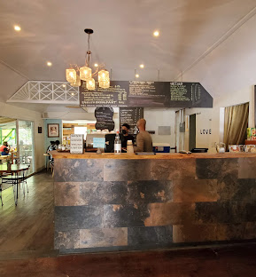 front counter of café with people stood behind and chairs/ tables to the left