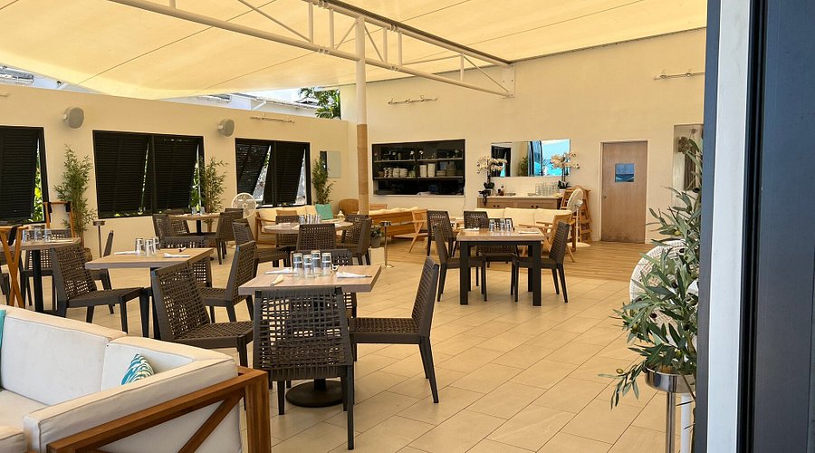 interior of calma beach club with lots ofc hairs and tables under a white canopy on the beach