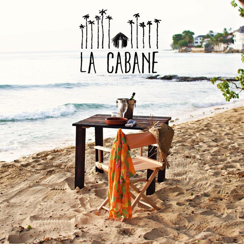 la cabane logo over a table and chair on the beach overlooking the sea with a shirt hanging off the chair