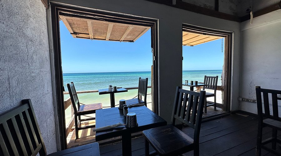 two sets of tables and chairs next to the sea in a café with sunny weather