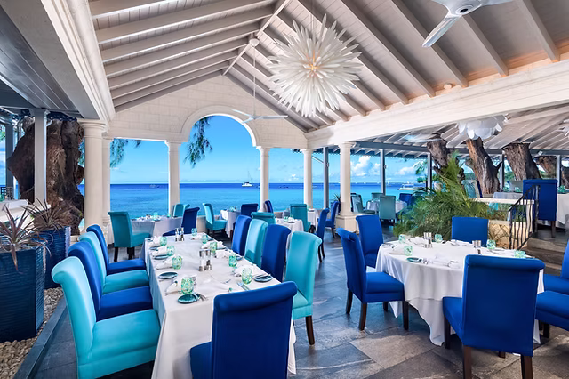 tides restaurant inside with blue chairs surrounding white tables under a white canopy next to the sea